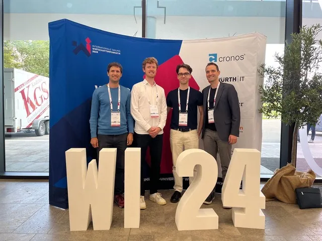 Vier Personen vor dem Banner der Internationalen Tagung Wirtschaftsinformatik 2024, davor große weiße Buchstaben „WI 24“